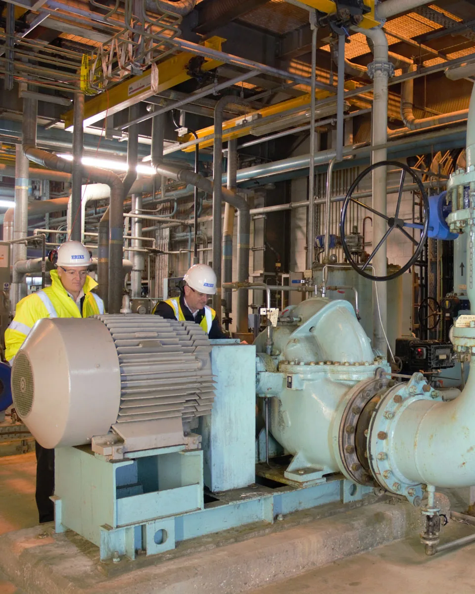 Two workers in hard hats and hi-vis assessing a pump in-situ